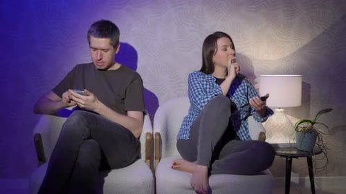 Man and Woman Sits on an Armchair and Using Mobile Phone in the Evening at Home