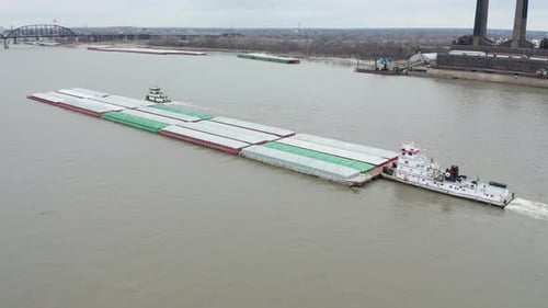 Aerial push in towards tugboat pushing heavy barge on Mississippi River.