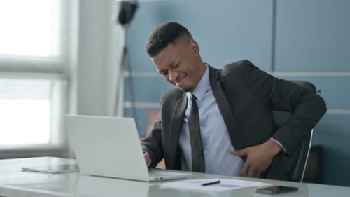 African Businessman having Back Pain while using Laptop in Office
