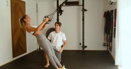 Strong sportswoman exercising with trainer on TRX straps