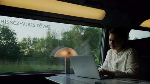 Woman Works on Laptop While Riding Train Sitting Near Window on Sunny Day