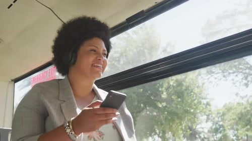 Happy plus size biracial woman using smartphone in bus