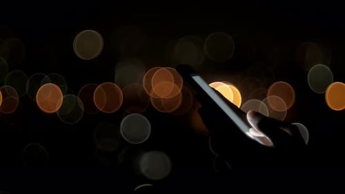 Hand Using Smartphone at Night With Bokeh Lights