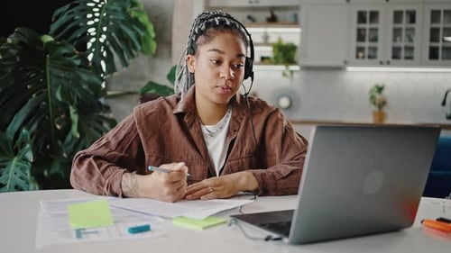 Junge afroamerikanische Frau im Headset mit Mikrofon, Video, chatte mit Arbeitgeber über Laptop