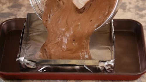 Un chef de cuisine verse de la pâte à gâteau au chocolat dans un moule carré pour la mettre au four