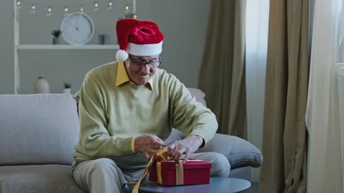 Senior Man Opening Christmas Gift Box at Home