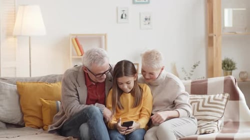 Girl on Couch with Grandparents Looking at Phone