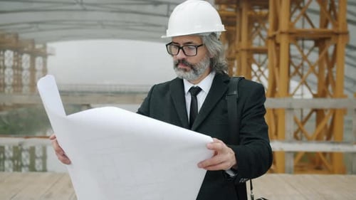 Construction Inspector Studying Blueprint and Looking Around Building Site Outdoors