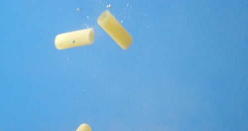 Dry Pasta Cannelloni Falls Under Water with Air Bubbles.