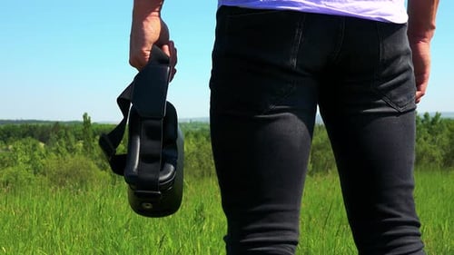 Young Handsome Man Holds Virtual Reality Glasses in Hand - Countryside in the Background