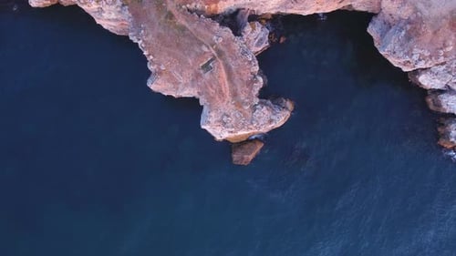 Top down aerial view of waves splash against rocky seashore, background. Flight over high cliffs of