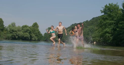Summer Joy Gruppe glücklicher Freunde, die Spaß beim Laufen und Planschen auf dem Fluss haben