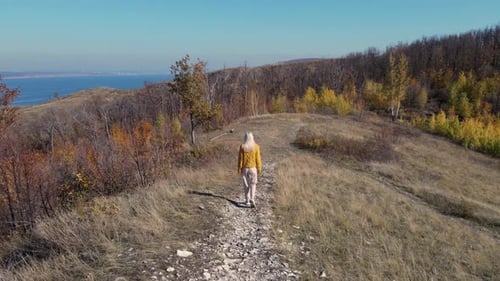 The drone follows a young beautiful woman walking along a mountain trail.