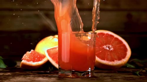 Un trozo de pomelo en cámara lenta cae en un vaso de zumo de pomelo con salpicaduras