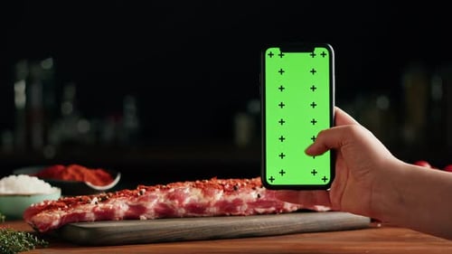 Hand Swiping Phone with Raw Ribs in Background
