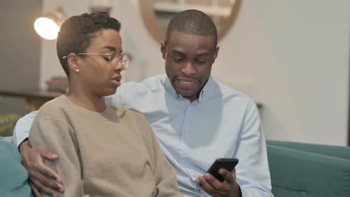 Couple Talking and Looking at Smartphone on Couch