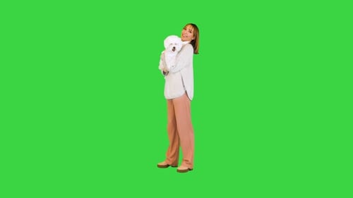 Charming Girl Standing with Bichon Frise in Her Hands on a Green Screen Chroma Key