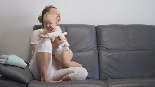 Glückliche junge Mutter umarmt Baby zu Hause auf dem Sofa