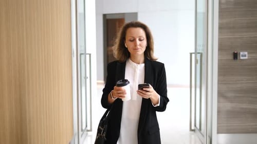 Woman Walking with Phone and Coffee in Office