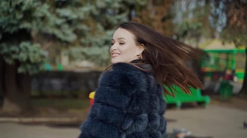 Attractive girl posing on camera. Pretty young woman in black fur coat standing in the park with cof