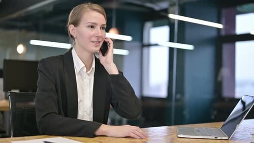 Happy Young Businesswoman Talking on Smartphone in Office