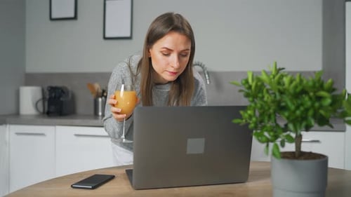 Woman Using Laptop in Modern Kitchen with Juice