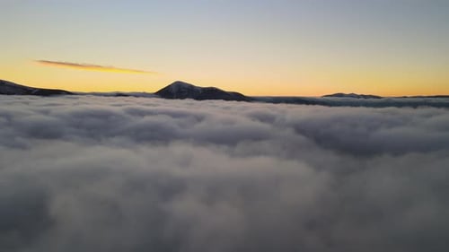 Aerial View of Vibrant Sunrise Over White Dense Clouds with Distant Dark Mountains on Horizon