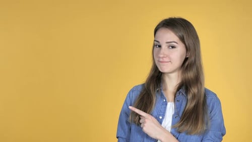 Young Woman Pointing to Left on Yellow Background