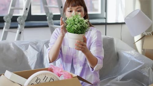 Woman Unpacks Moving Boxes, Holds Potted Plant