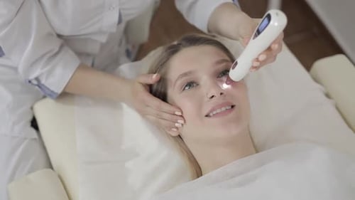 Primer plano de las manos del médico con un aparato para cosmetología láser que hace un tratamiento para jóvenes