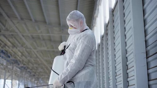 Mann gekleidet, weißer Schutzoverall, der die Oberfläche besprüht, antibakterielles Desinfektionsspray, während