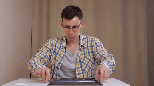 Mann mit Brille zerlegt einen Laptop, während er an einem weißen Tisch sitzt
