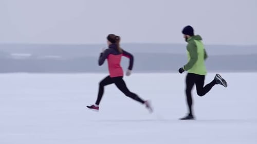 Athletic Couple Running in Snowy Field on Winter Day