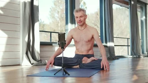 Yoga-Mann sitzt im Schneidersitz auf dem Boden und trainiert online vor dem Telefon