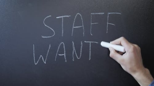 Staff wanted written on chalkboard. Male hands writes staff wanted with chalk on blackboard.