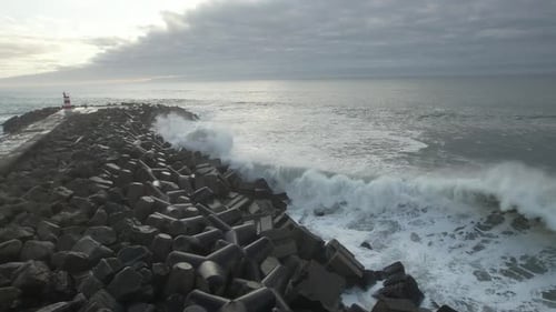 Waves Crashing on Rock Pier with Distant Lighthouse