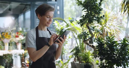Young Entrepreneur Touching Tablet Screen Looking at Flowers in Florist's Shop