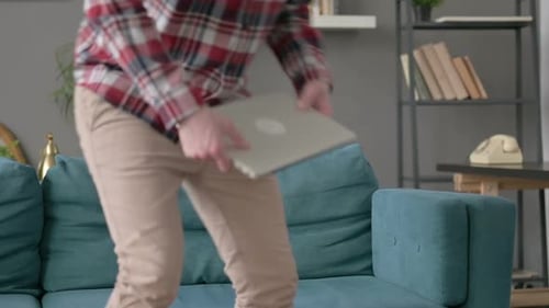 Man Opens Laptop on Couch Indoors