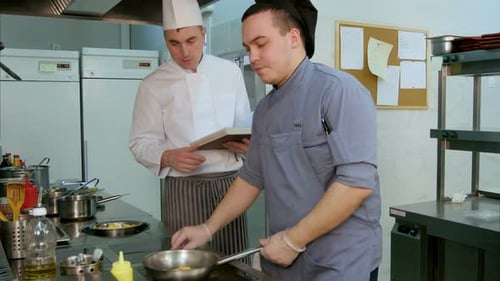 Chef con libro de cocina instruyendo al aprendiz de cocinero cómo freír camarones