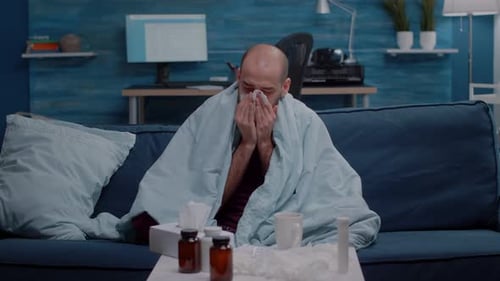Man Sick With Flu Blowing Nose On Sofa