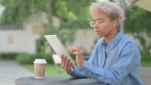 Attractive Young African Woman Using Tablet in Outdoor Cafe