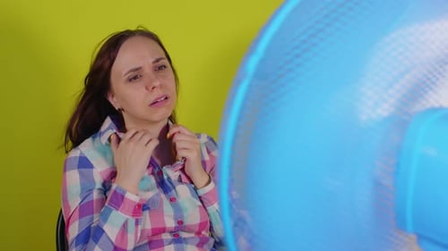Close Up of Young Woman Sitting on Chair in Front of Fan on Yellow Background