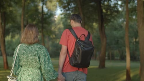 30s Couple Holding Hands Walking in Green Park