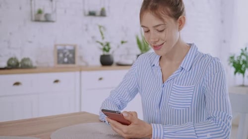 Woman Using Smartphone at Kitchen Table