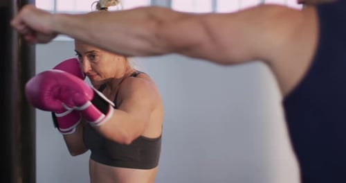 Caucasian female boxer wearing boxing gloves training with punching bag with male trainer at the gym