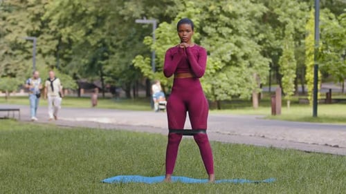 Athletic Woman Doing Squats with Resistance Band in Park