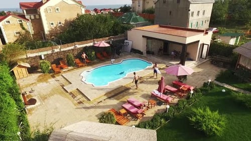 Flyover Footage From Drone in Slowmotion of Four Caucasian Males Jumping Into Pool with Blue Water