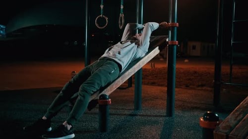 Un homme est allongé sur un équipement de sport de plein air dans un parc et entraîne les jambes et l'abdomen