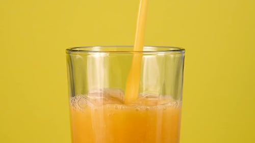 Orange Juice Pouring Into Glass on Yellow Background
