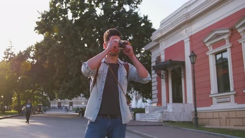 Young Attractive Handsome Man Tourist with Backpack Taking Photos on Vintage Camera in Old City